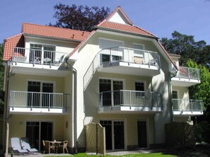 A multi-story residential building with balconies, a covered patio area with seating, and a red-tiled roof.