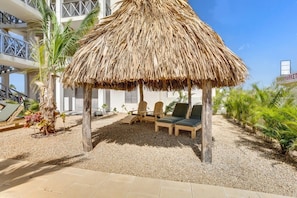 A thatched-roof outdoor seating area with lounge chairs and a palm tree.