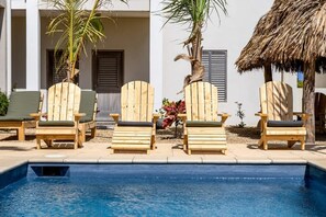 A poolside area with wooden lounge chairs and a thatched roof structure. - Belnem Breeze Tres with a mature palm garden and refreshing shared pool (Kralendijk)