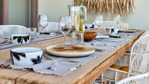 Mesa de comedor dispuesta con platos, vasos y una jarra, rodeada de sillas de mimbre.