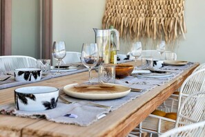 A dining table set with plates, glasses, and a pitcher, surrounded by wicker chairs. - Belnem Breeze Tres with a mature palm garden and refreshing shared pool (Kralendijk)