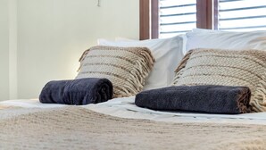 Una cama con un edredón texturizado, dos almohadas con estampado a rayas y una ventana con persianas.