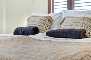 A bed with a textured blanket, two pillows with a striped pattern, and a window with blinds. - Belnem Breeze Tres with a mature palm garden and refreshing shared pool (Kralendijk)