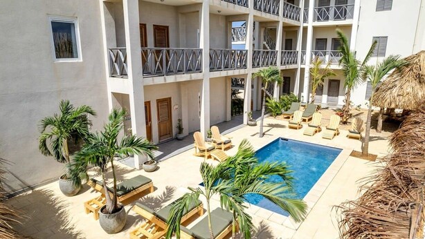 Un edificio de varios pisos con piscina, zona de estar al aire libre y palmeras.
