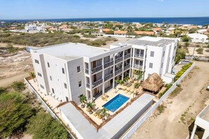 A multi-story hotel with a rooftop pool, surrounded by greenery and a view of the sea. - Belnem Breeze Tres with a mature palm garden and refreshing shared pool (Kralendijk)