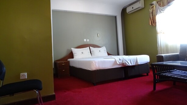 A hotel room with a bed, a chair, a nightstand, and a window with curtains. - Ceamo Prestige Lodge (Makutano)