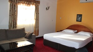 A hotel room with a bed, a sofa, a small table, and a window with curtains. - Ceamo Prestige Lodge (Makutano)