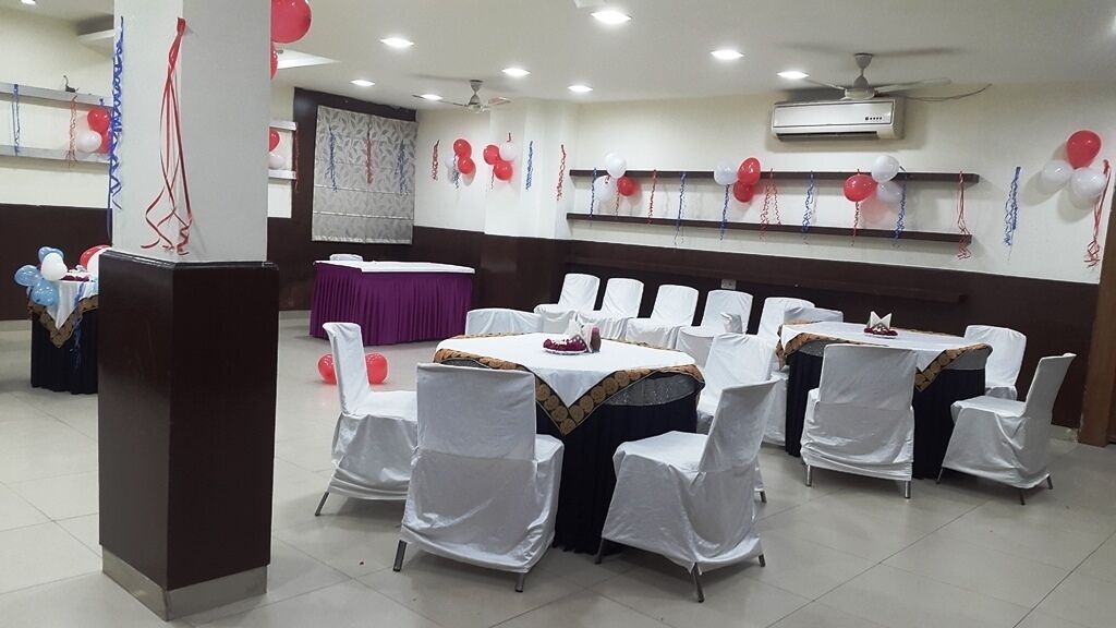 Une salle de banquet avec des tables rondes recouvertes de nappes blanches et des chaises blanches.