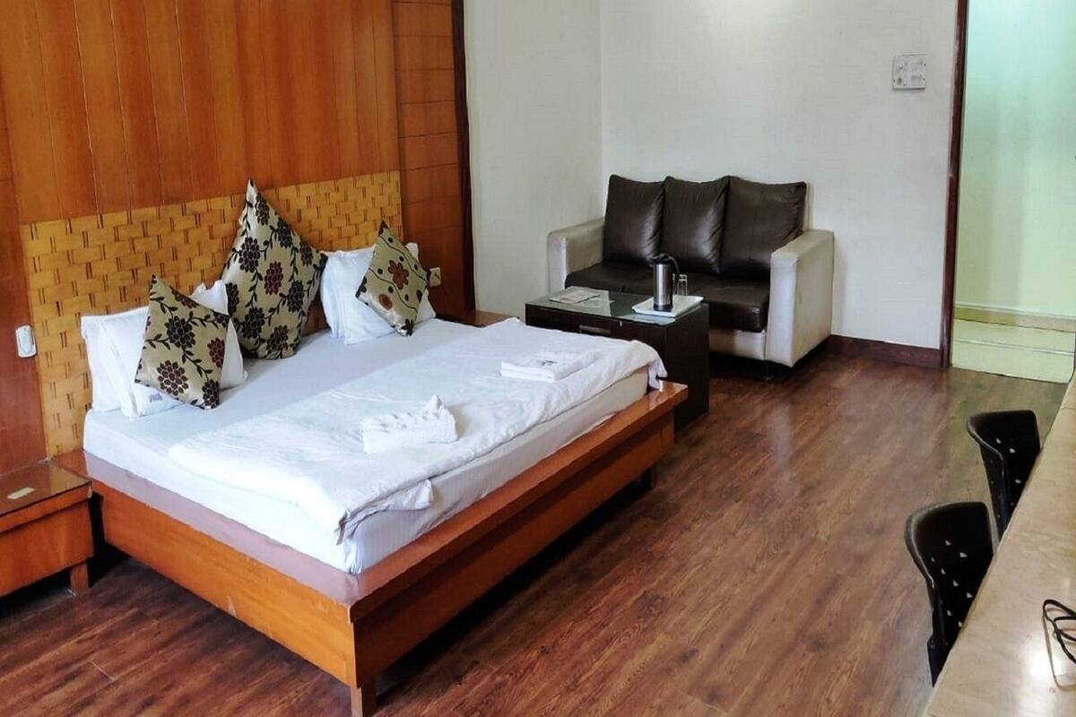 Une chambre d’hôtel avec un lit en bois, un canapé, une table basse et une table à manger avec des chaises.