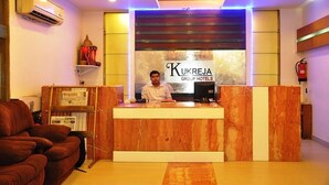 Un mostrador de recepción en Kukreja Group Hotels con diseño de mármol, un hombre detrás y un sofá rojo a la izquierda.