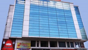 Un hotel con un amplio frente de vidrio, con letreros que dicen 'Miss Boutique' y 'PRL Knit' en la planta baja, y un letrero de 'Mandakini Plaza' en la parte superior.