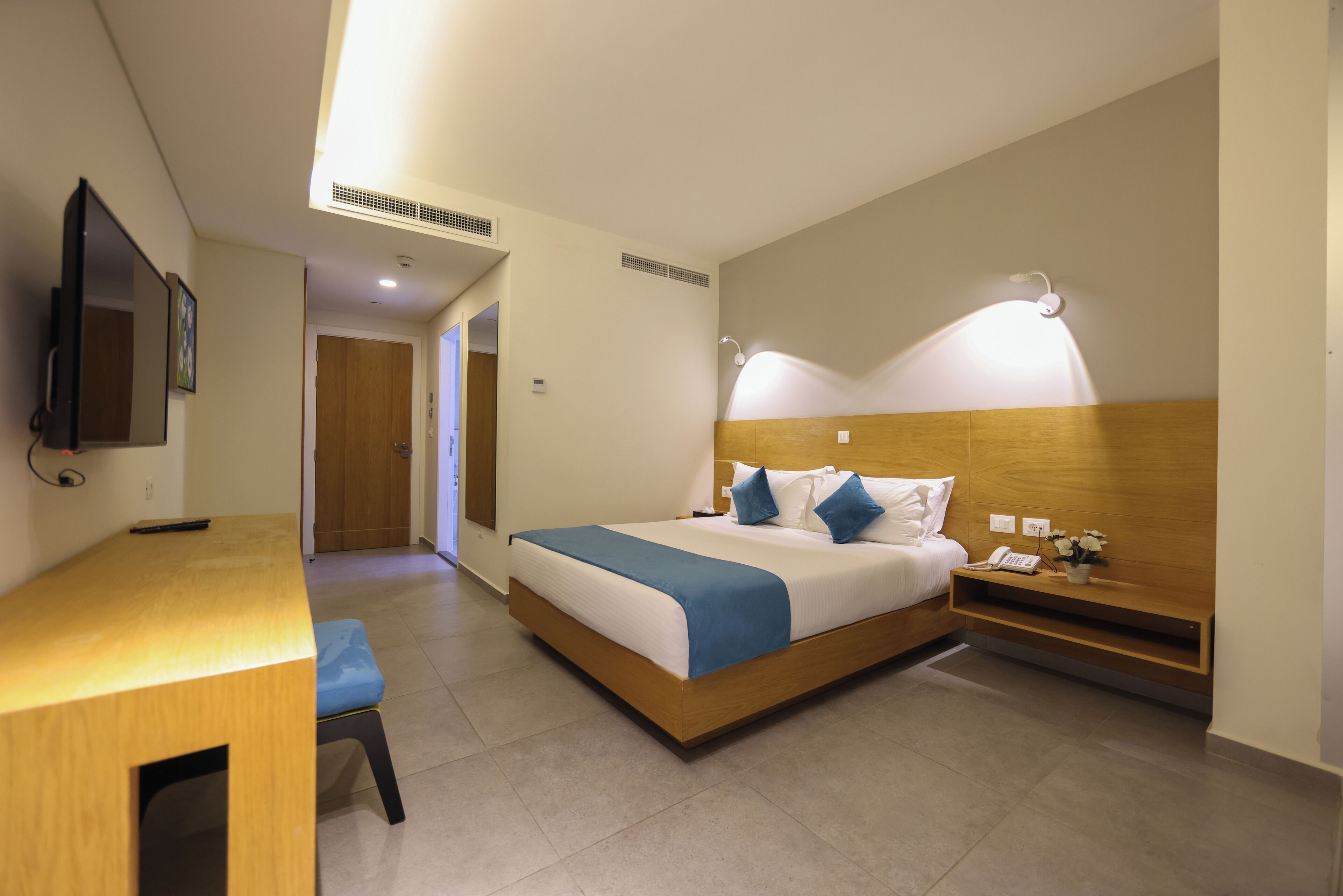 A bedroom with a bed, bedside table, lamp, and a TV mounted on the wall.