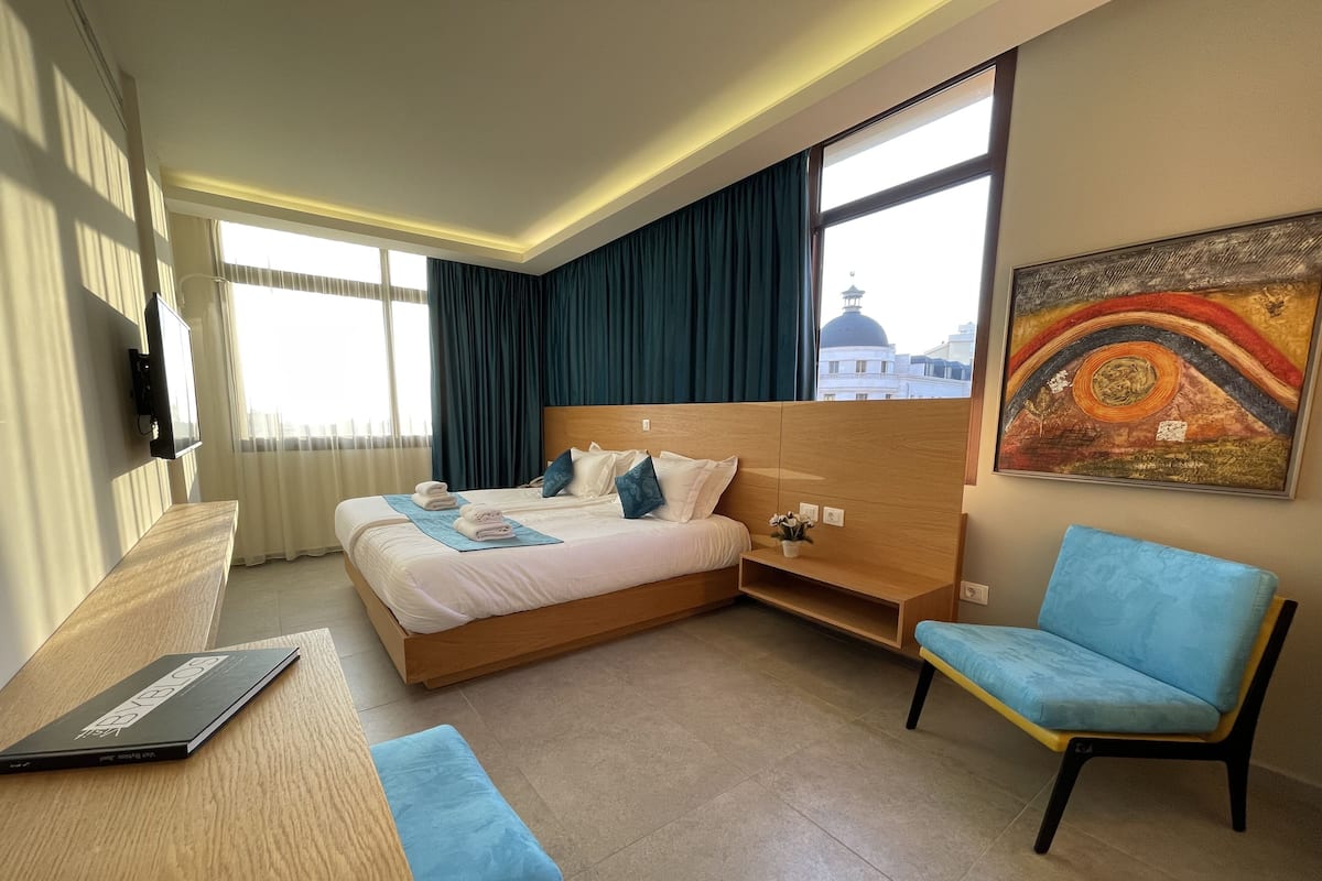 A hotel room with a bed, a desk, a chair, and a painting on the wall.