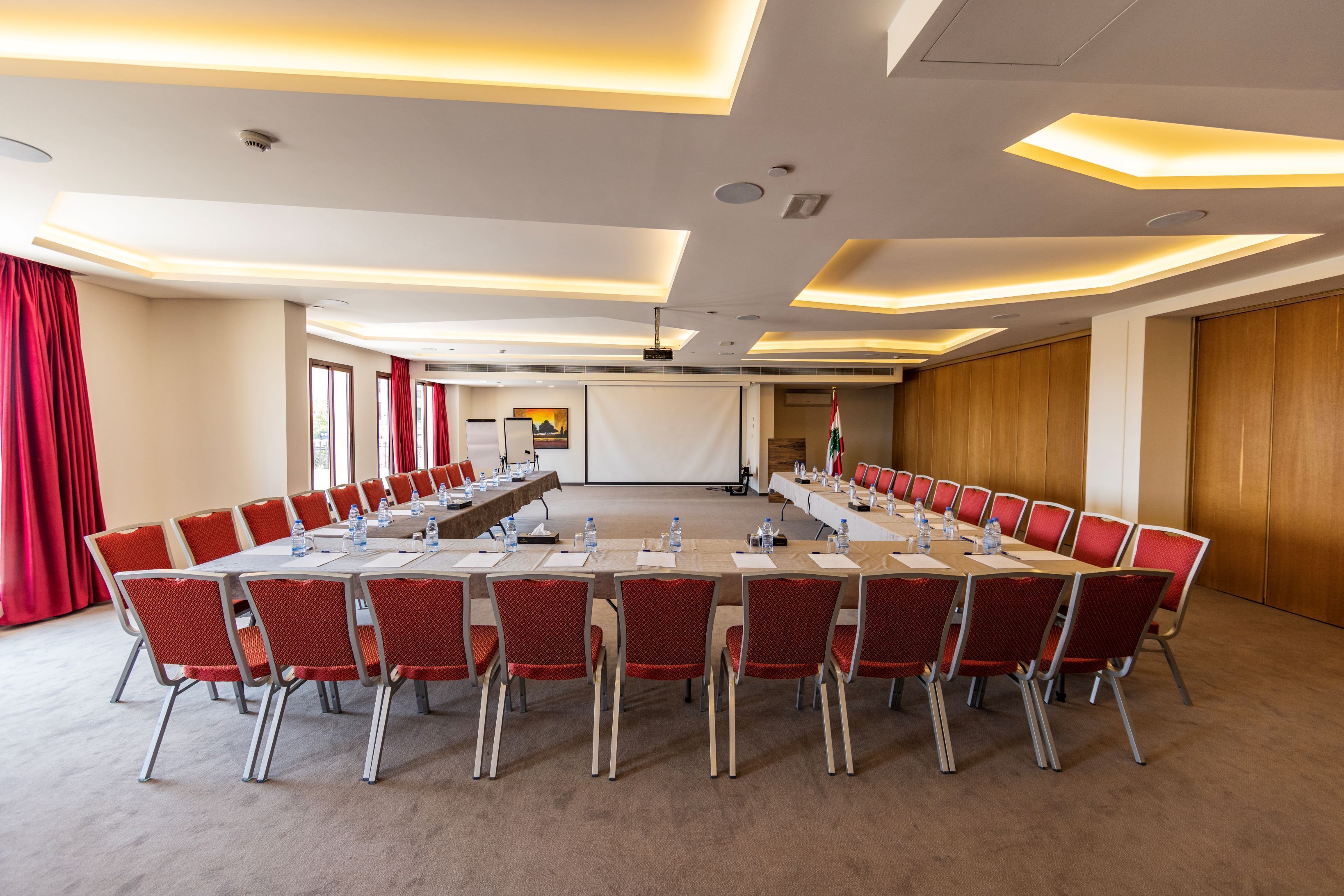 A conference room with a long table, red chairs, and a projector screen.