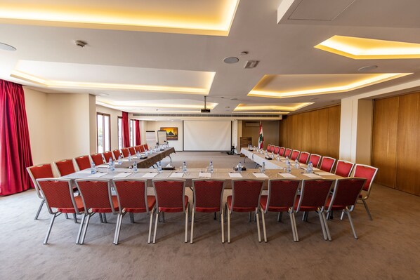 A conference room with a long table, red chairs, and a projector screen.