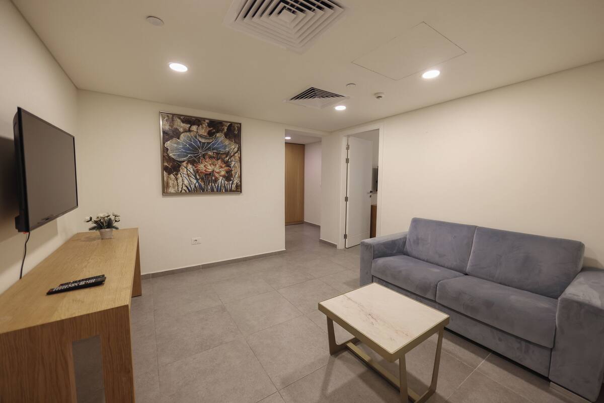 A modern living room with a grey sofa, a wooden coffee table, a flat-screen TV, and a painting on the wall.
