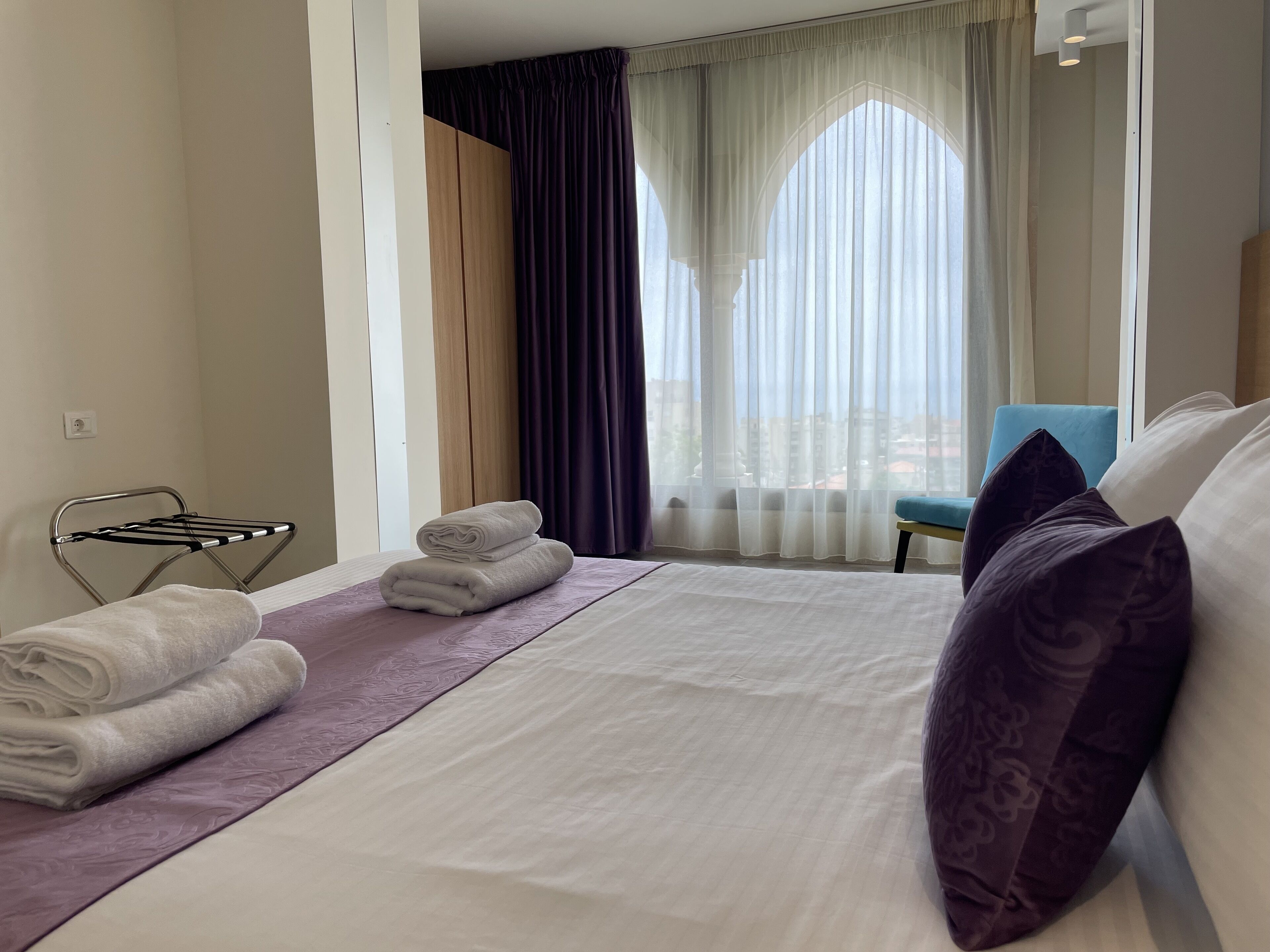 A hotel room with a neatly made bed, a chair, and a window with curtains.