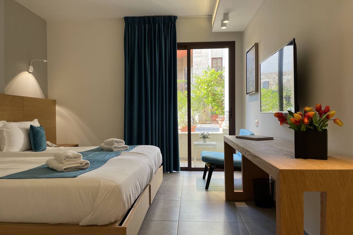 A modern hotel room with a bed, a desk, a chair, a TV, and a view of the outdoors.