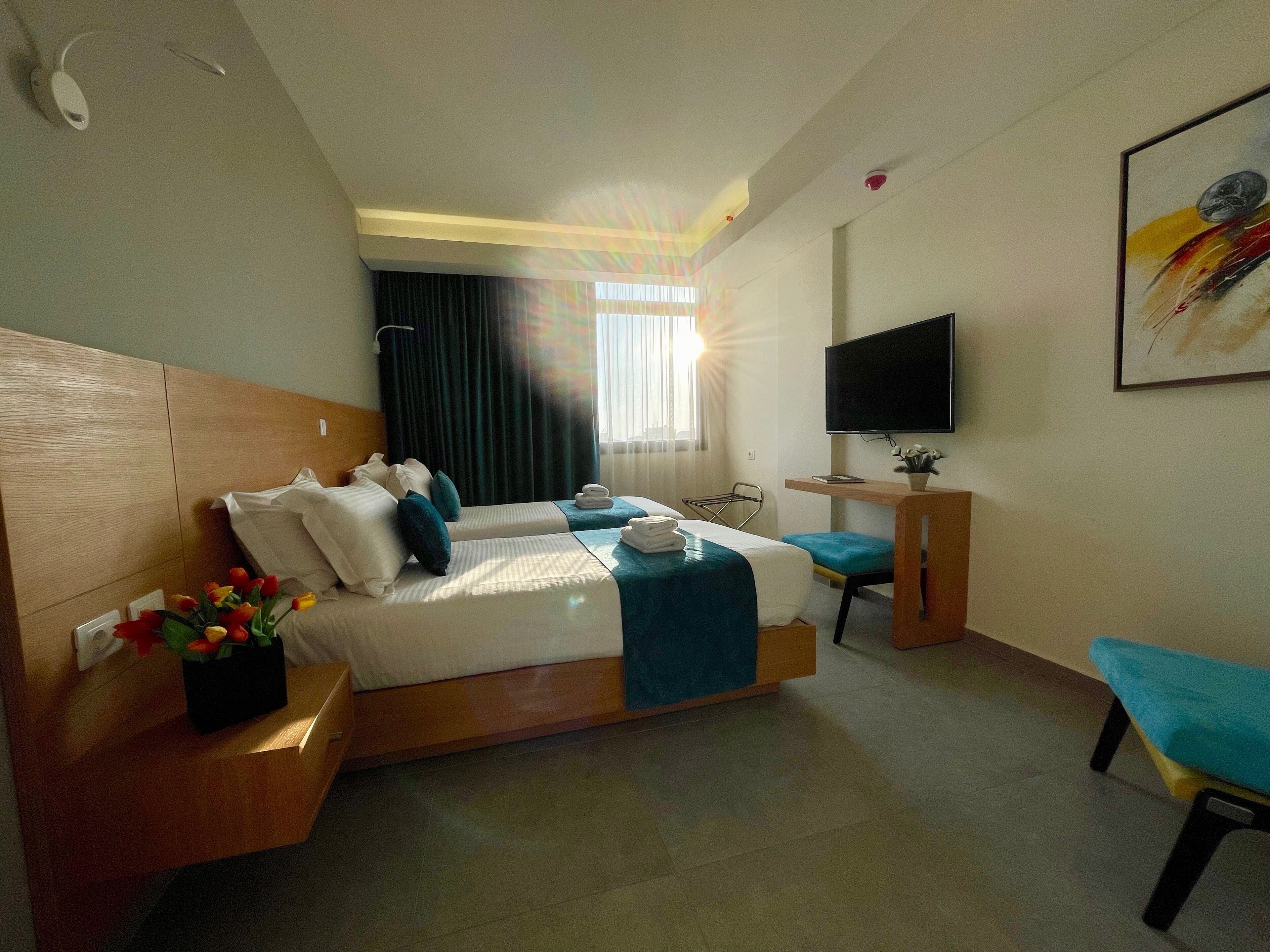 A hotel room with a large bed, a desk, a chair, a TV, and a painting on the wall.
