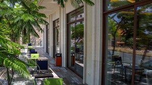 Een terras met tafels en stoelen, grote ramen en planten.