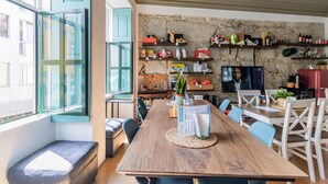 A dining area with a wooden table, chairs, and a stone wall with shelves displaying shoes and other items. - Invictus Hostel (Porto)