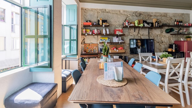 A dining area with a wooden table, chairs, and a stone wall with shelves displaying shoes and other items. - Invictus Hostel (Porto)