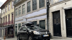 A black car parked on a cobblestone street in front of a building with a hostel sign. - Invictus Hostel (Porto)