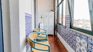 A narrow corridor with a row of lockers, a chair, and a window with a view of buildings. - Invictus Hostel (Porto)