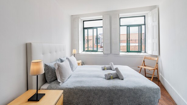 A bedroom with a bed, bedside table, lamp, and a chair. - Invictus Hostel (Porto)