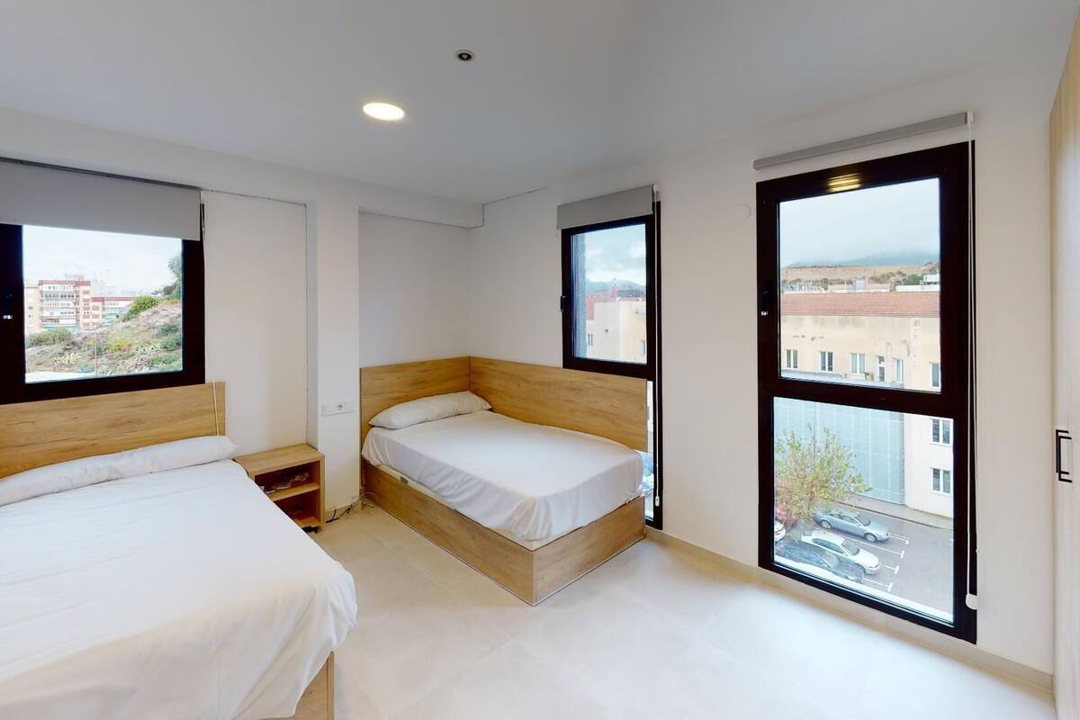 Een moderne slaapkamer met twee bedden, grote ramen en uitzicht op de stad.