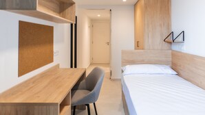 Een moderne slaapkamer met een houten bureau, een grijze stoel, een bed met wit beddengoed en ingebouwde houten planken.
