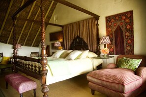 A traditional bedroom with a four-poster bed, a wooden bench, a cushioned chair, and a decorative tapestry. - Olepangi Farm (Nanyuki)