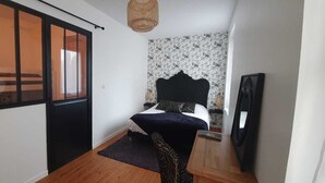A bedroom with a bed, a wooden floor, a black headboard, a patterned wallpaper, a woven light fixture, and a framed picture on the wall. - O Tour's Angels "Rabelais" (37000 TOURS)