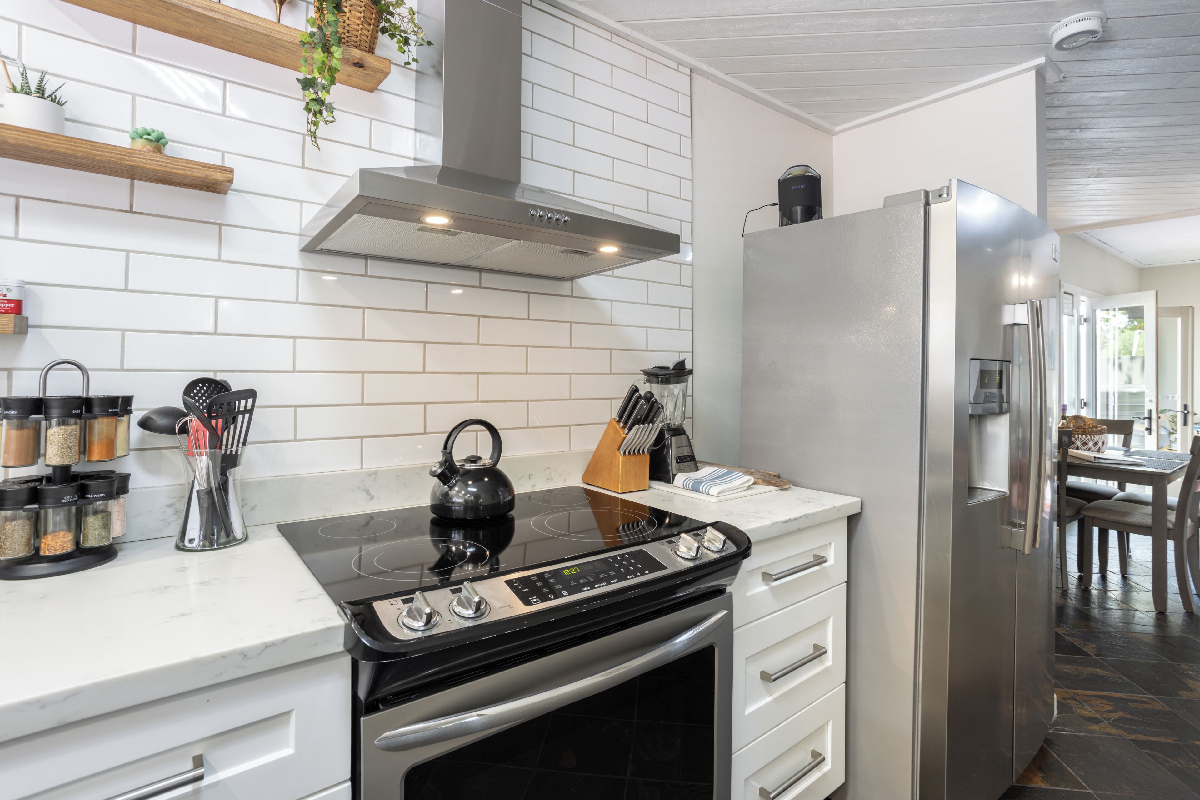 A modern kitchen with white tiles, stainless steel appliances, and a black induction cooktop.