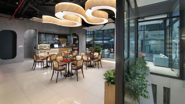 Een modern café met een strak, minimalistisch design, met een centraal zitgedeelte met tafels en stoelen, een bar en grote ramen met uitzicht op de stad.