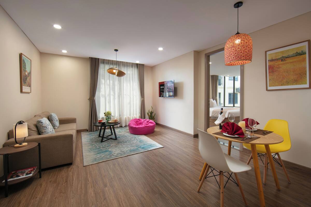 Una sala moderna con un sofá, un sillón de peluche rosa, una mesa de comedor con sillas y un televisor en la pared.