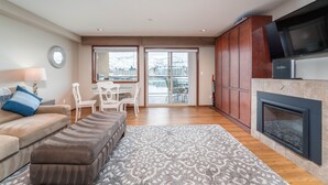 A modern living room with a sofa, ottoman, patterned rug, wooden flooring, a fireplace, and a dining area with chairs and a table. - Grandview 624 Waterfront condo on Lake Chelan (Chelan)