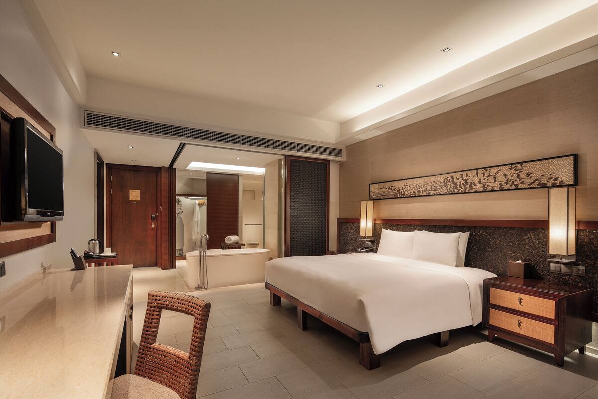 Une chambre d’hôtel comprenant un grand lit, un bureau, une chaise, une télévision, une salle de bain et un élément décoratif mural.