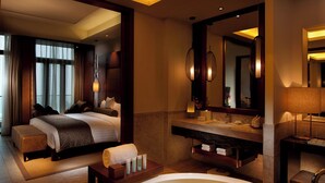 Une chambre d’hôtel dotée d’une grande baignoire remplie d’eau et ornée de fleurs flottantes, d’un lit offrant une vue sur la pièce et d’une salle de bain avec un grand miroir et des équipements modernes.