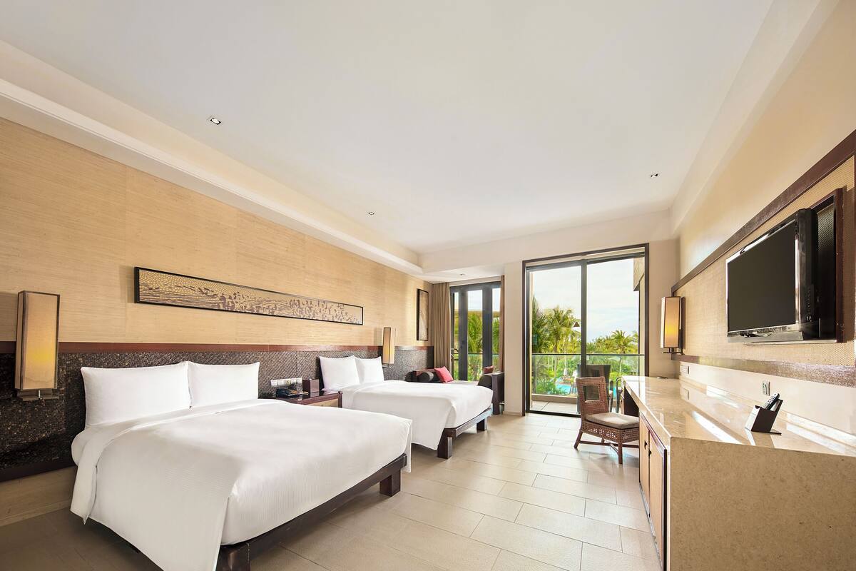 Une chambre d’hôtel avec deux lits, une grande télévision, un balcon avec vue et une salle de bain équipée d’un lavabo et d’un miroir.