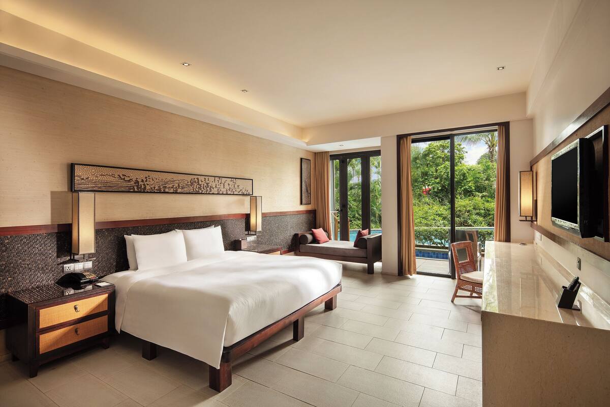 Une chambre d’hôtel spacieuse dotée d’un grand lit, d’un coin salon, d’un balcon avec vue sur la piscine et d’une télévision à écran plat.