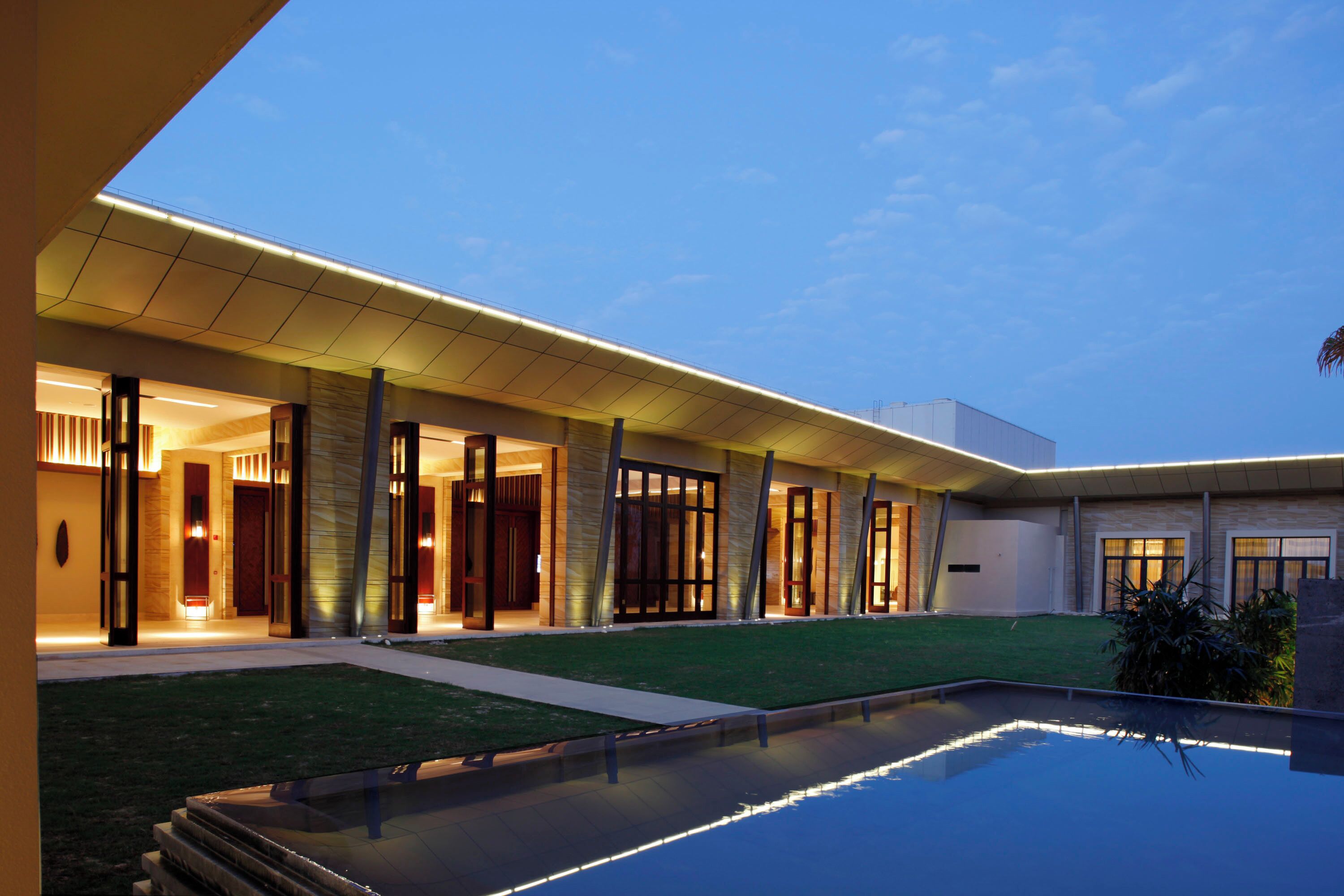 A modern hotel with a swimming pool, covered outdoor area, and well-lit entrance.