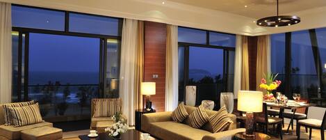 A spacious living room with a large window overlooking the ocean, a sofa, a coffee table, and a dining area with a table and chairs.