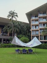 Una carpa con diseño floral montada sobre una zona de césped, con sillas plegables azules en primer plano.