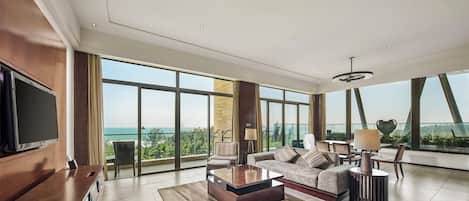 A spacious living area with a large flat-screen TV, a sofa set, a coffee table, and a view of the ocean through expansive windows.