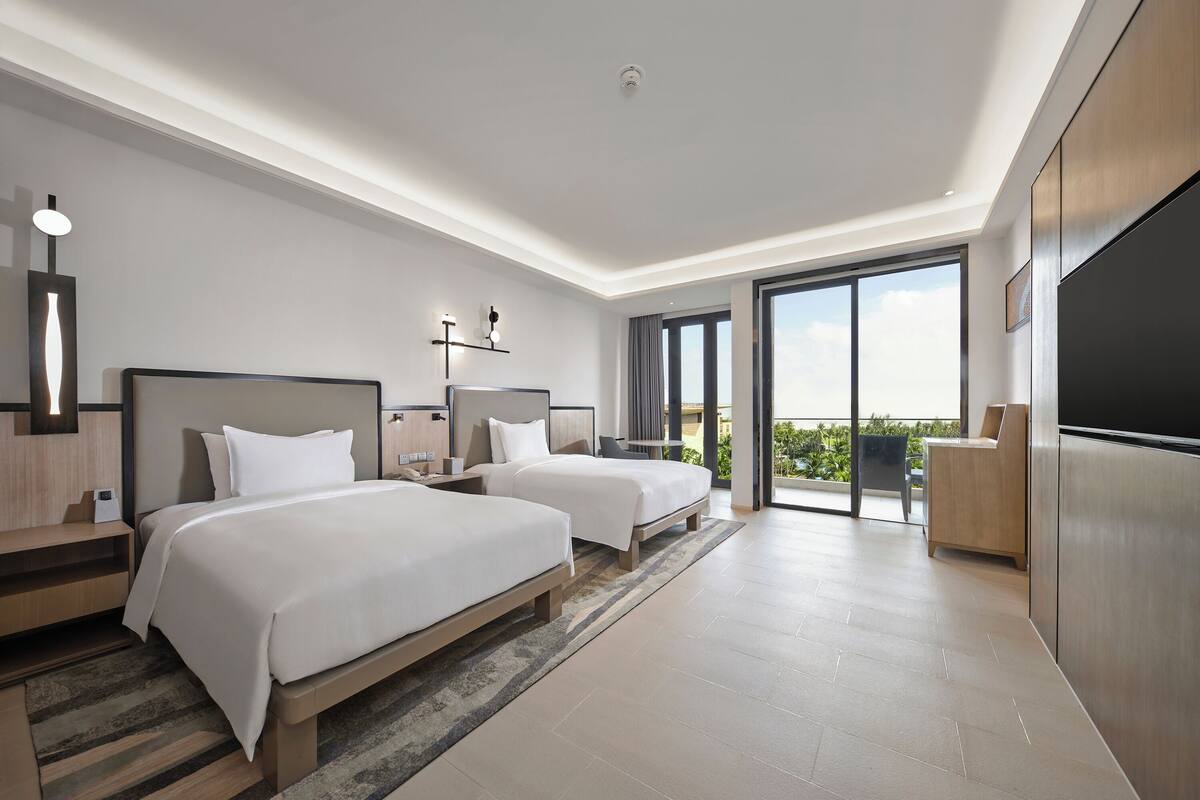 Une chambre d’hôtel moderne avec deux lits, une grande porte-fenêtre coulissante donnant sur le balcon et un téléviseur à écran plat.