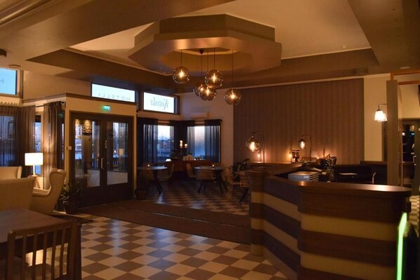 A hotel lobby with a checkered floor, a reception desk, and a seating area with tables and chairs.