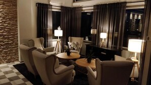 Een hotelkamer met een zwart-wit geruite vloer, een accentmuur van steen, een zithoek, een salontafel en lampen.
