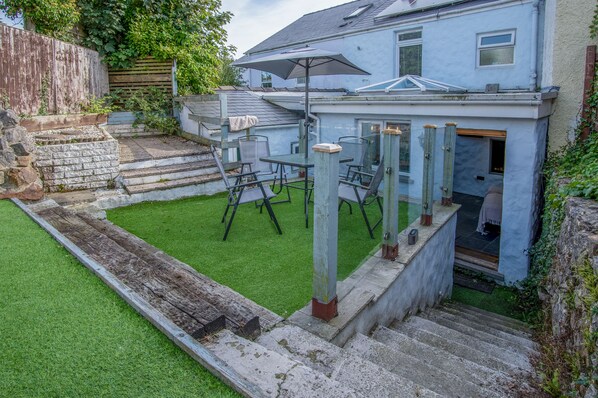 A backyard with a patio area, outdoor seating, and a house with a light blue exterior.
