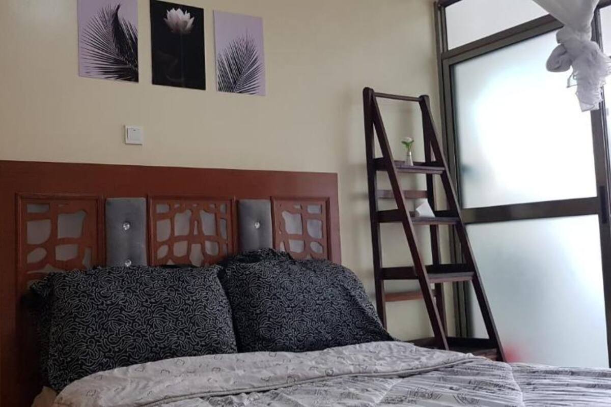 A bedroom with a wooden headboard, patterned pillows, a bed with a white and gray bedspread, and a window with a view of the outside.